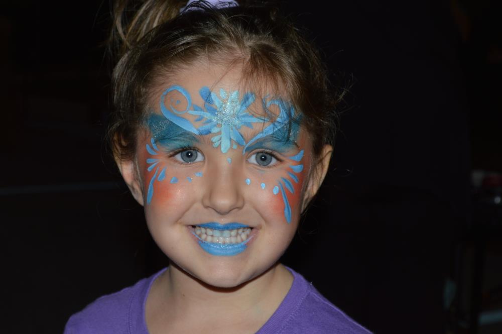 Girl smiles for camera with blue facepaint design on face